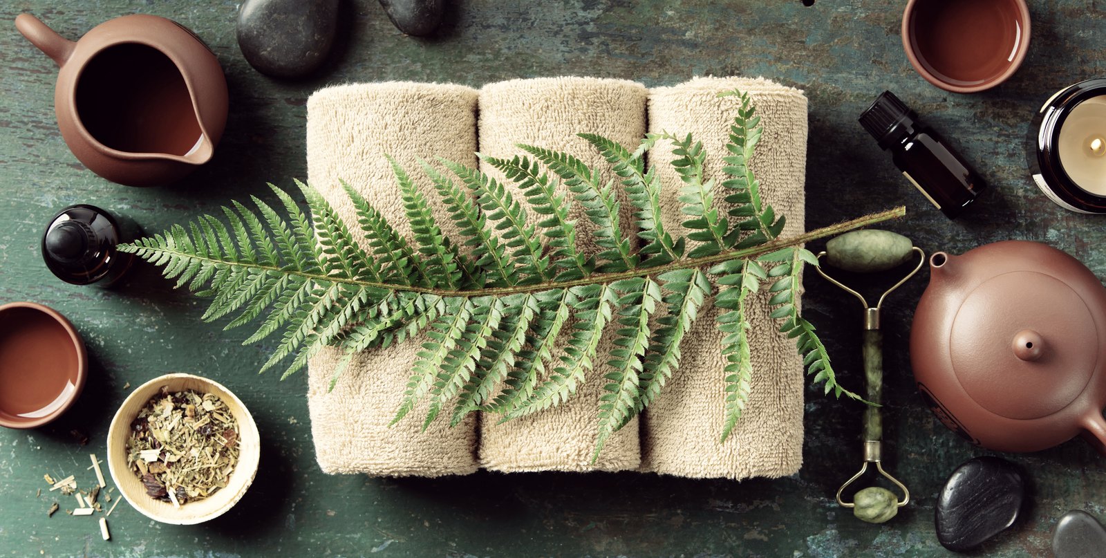 Spa flatlay with folded towels, herbal tea, oils and a jade roller
