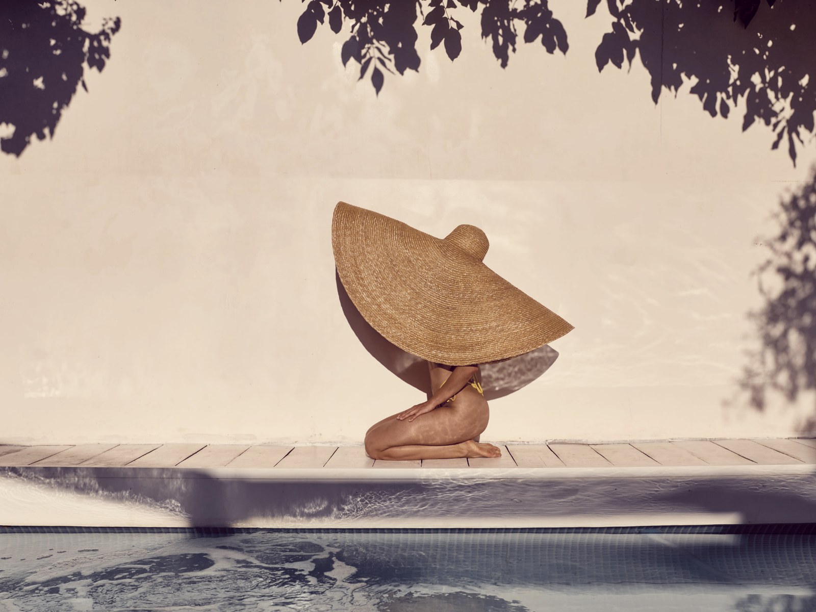 Guest in a wide straw hat sitting beside a sunlit resort pool